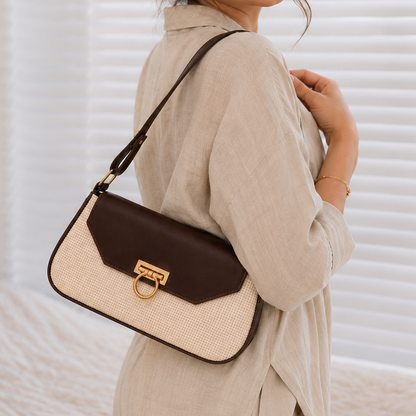 Woman holding a beige and brown handbag in a room with white walls and bedding.